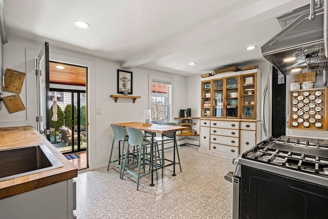 kitchen with baseboards, beam ceiling, gas stove, and a healthy amount of sunlight