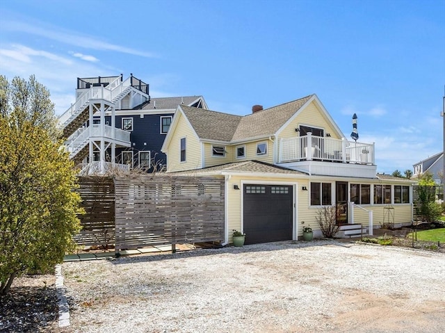 view of front of house featuring a garage, a balcony, a sunroom, a shingled roof, and driveway
