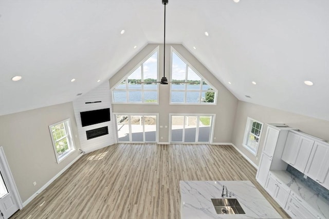 unfurnished living room featuring baseboards, high vaulted ceiling, light wood-style flooring, a fireplace, and a sink