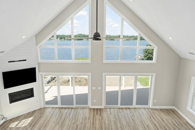 unfurnished living room featuring baseboards, a water view, wood finished floors, and a fireplace