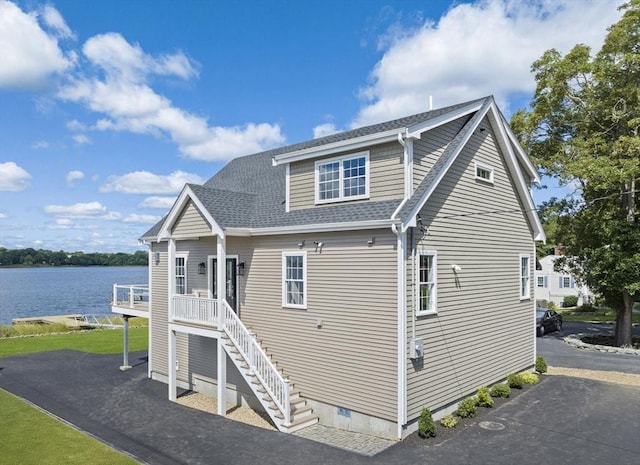 exterior space with stairway, a deck with water view, and roof with shingles