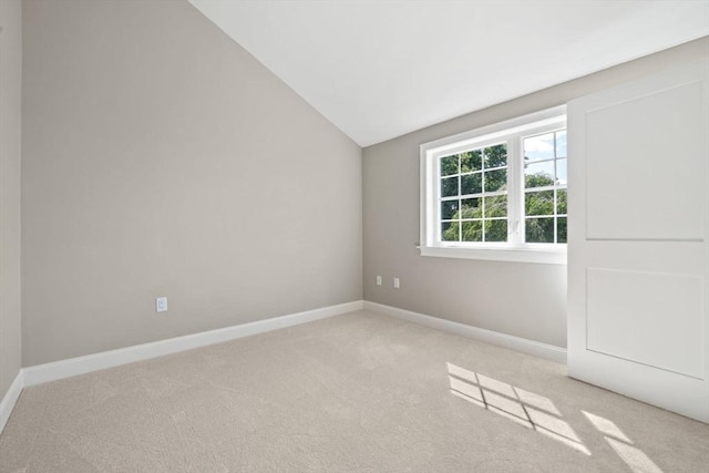 carpeted spare room featuring vaulted ceiling and baseboards