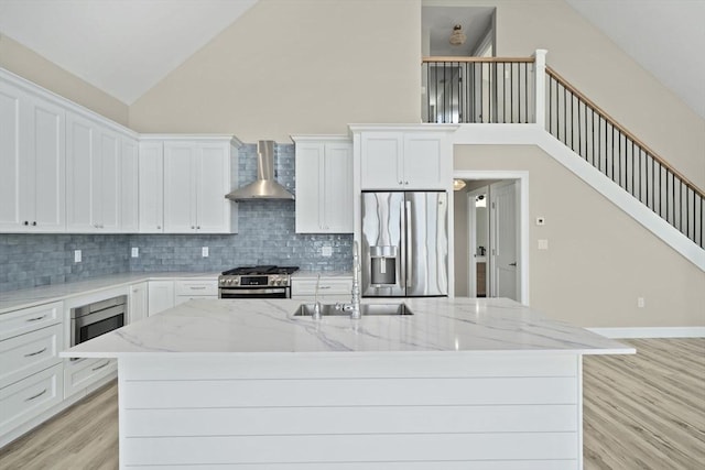 kitchen featuring a center island with sink, stainless steel appliances, light wood-style floors, white cabinetry, and wall chimney exhaust hood