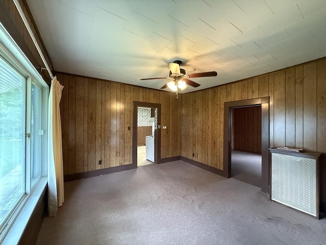 carpeted spare room with ceiling fan, wood walls, and baseboards