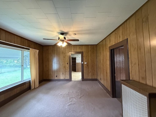 empty room featuring ceiling fan, wood walls, baseboards, and light colored carpet