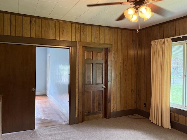 spare room featuring wood walls, ceiling fan, and light carpet