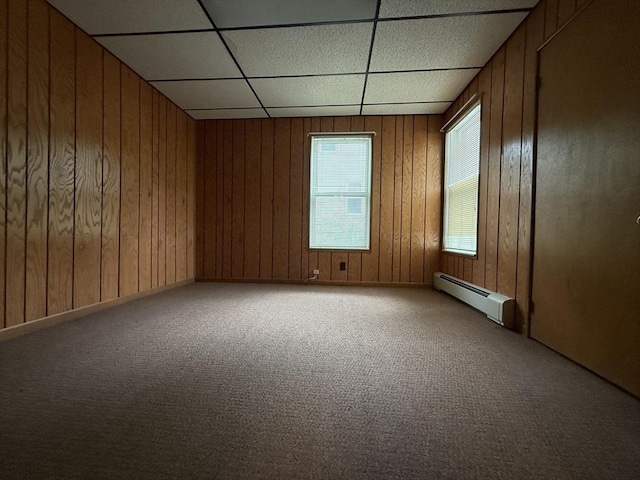 carpeted spare room with baseboard heating, a paneled ceiling, and wooden walls