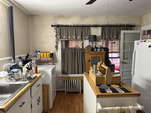 clothes washing area featuring radiator, dark wood-style flooring, washer and clothes dryer, a sink, and a ceiling fan