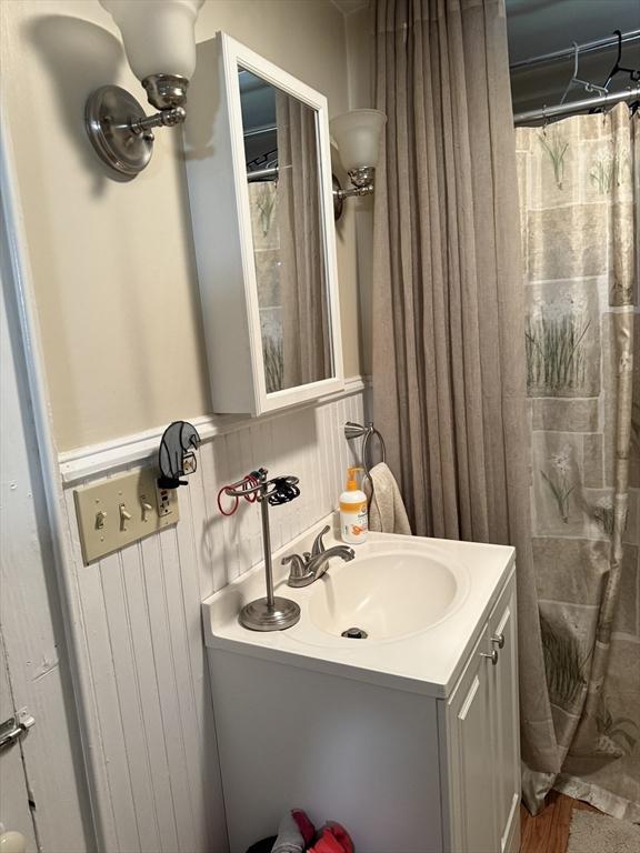 full bath featuring vanity, wainscoting, and wood finished floors