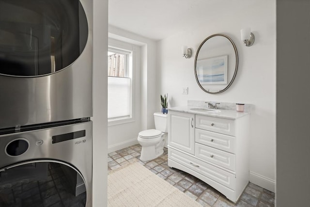 bathroom featuring vanity, toilet, baseboards, and stacked washer / drying machine