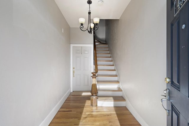 foyer entrance featuring a chandelier, stairway, baseboards, and wood finished floors