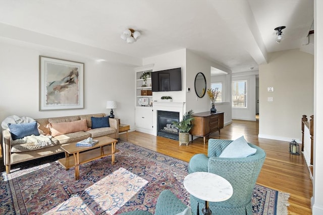 living room featuring a glass covered fireplace, baseboards, and wood finished floors