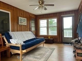 living area featuring ceiling fan, wooden walls, and light hardwood / wood-style flooring