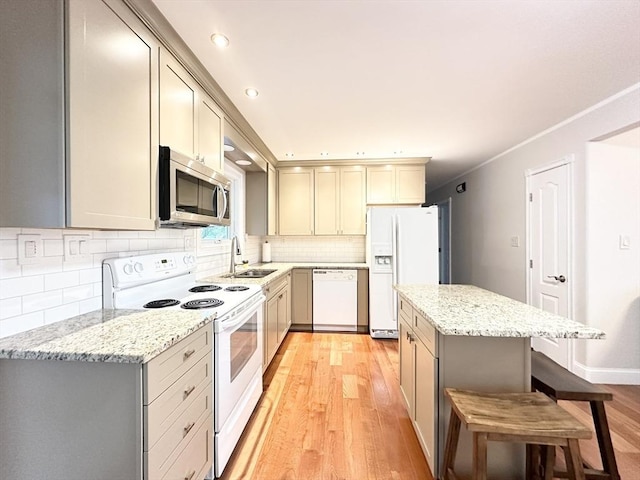 kitchen featuring sink, light stone counters, light hardwood / wood-style floors, white appliances, and a breakfast bar area