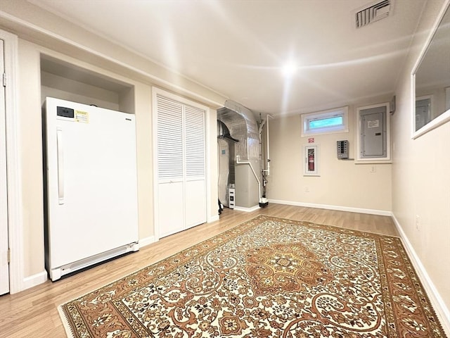 basement featuring electric panel, hardwood / wood-style floors, and white fridge