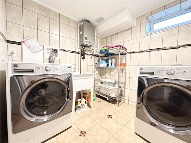 washroom with light tile patterned floors, washing machine and dryer, tankless water heater, and tile walls