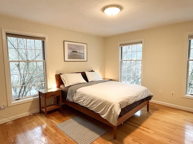 bedroom with multiple windows, baseboards, and light wood finished floors