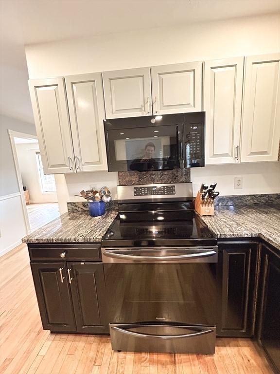 kitchen featuring stainless steel electric range oven, dark stone countertops, white cabinets, black microwave, and light wood-type flooring