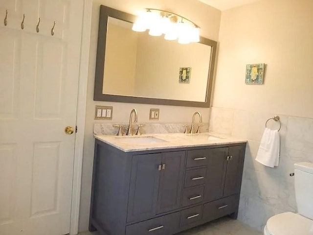 full bath with double vanity, toilet, tile walls, and a sink