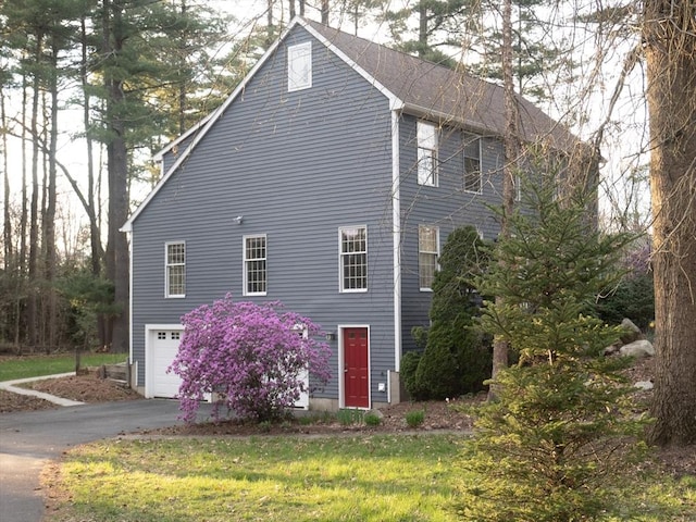 view of side of property featuring aphalt driveway, a lawn, and an attached garage