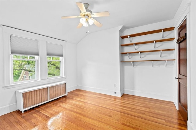 unfurnished bedroom featuring radiator, light wood-style floors, baseboards, lofted ceiling, and ceiling fan