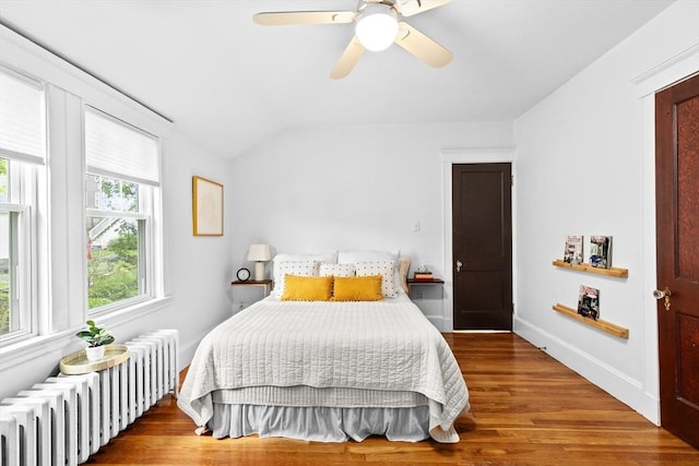 bedroom featuring radiator heating unit, wood finished floors, lofted ceiling, a ceiling fan, and baseboards