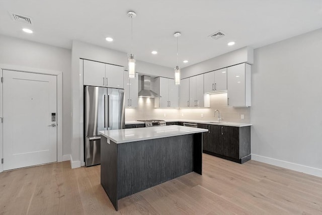 kitchen featuring wall chimney range hood, a sink, stainless steel refrigerator, and visible vents