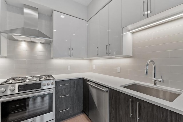 kitchen with light countertops, a sink, tasteful backsplash, appliances with stainless steel finishes, and wall chimney range hood