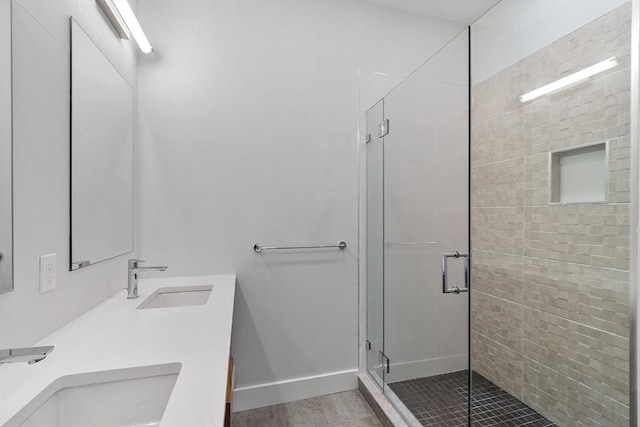 full bathroom with double vanity, a sink, baseboards, and a shower stall