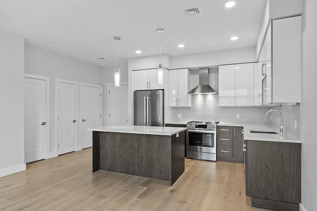 kitchen featuring white cabinets, wall chimney exhaust hood, light countertops, and appliances with stainless steel finishes
