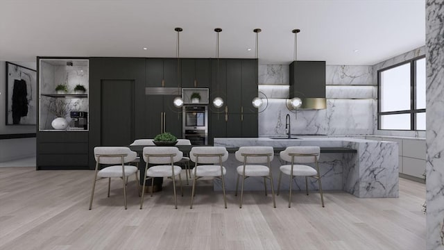 kitchen with sink, a center island with sink, pendant lighting, stainless steel double oven, and light hardwood / wood-style floors