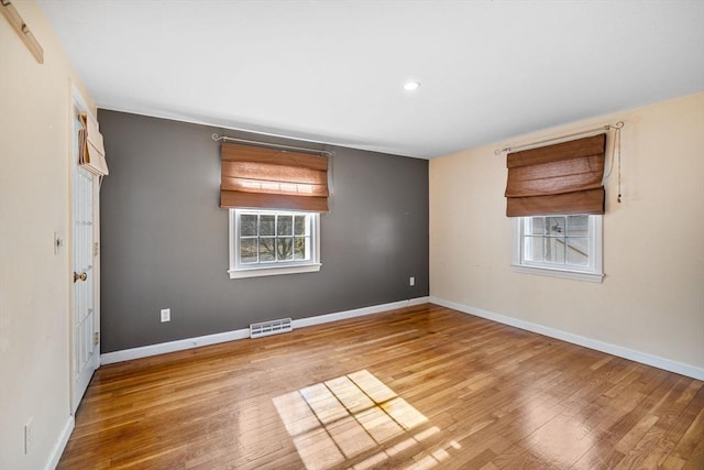 empty room with baseboards, visible vents, wood finished floors, and a wealth of natural light