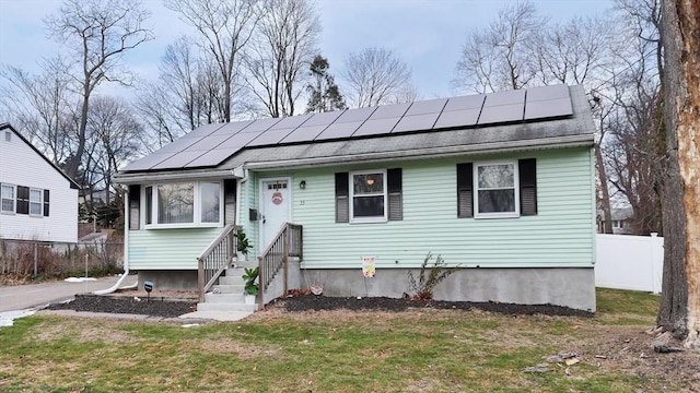 bungalow-style home with a front lawn, a shingled roof, fence, and roof mounted solar panels