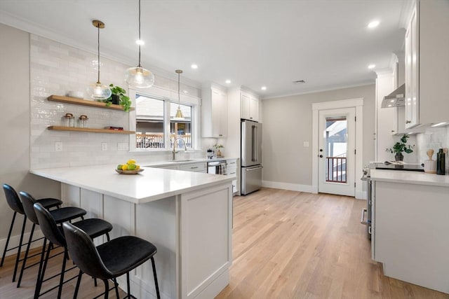 kitchen featuring white cabinetry, stainless steel appliances, kitchen peninsula, decorative light fixtures, and a kitchen bar