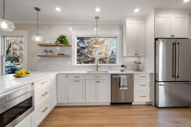 kitchen featuring white cabinets, hanging light fixtures, light hardwood / wood-style flooring, decorative backsplash, and appliances with stainless steel finishes