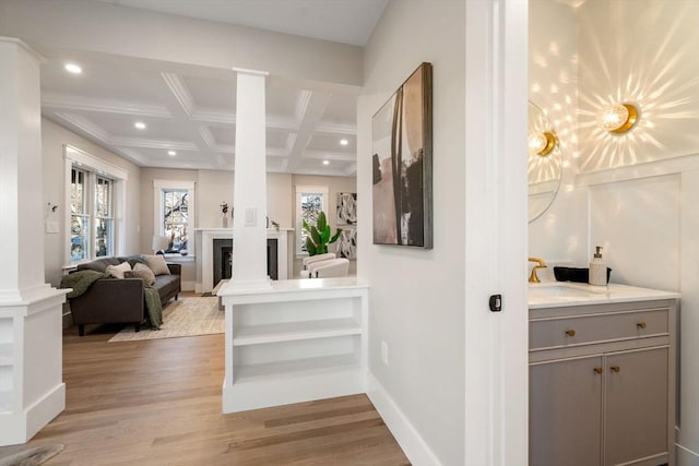 hallway with beam ceiling, sink, coffered ceiling, decorative columns, and light hardwood / wood-style floors