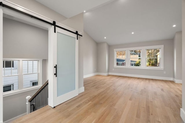 unfurnished living room featuring a barn door, vaulted ceiling, and light wood-type flooring