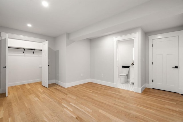 unfurnished bedroom featuring ensuite bath and light wood-type flooring