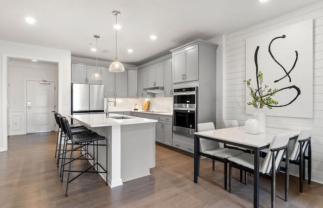 kitchen featuring gray cabinetry, stainless steel appliances, a sink, a breakfast bar area, and recessed lighting