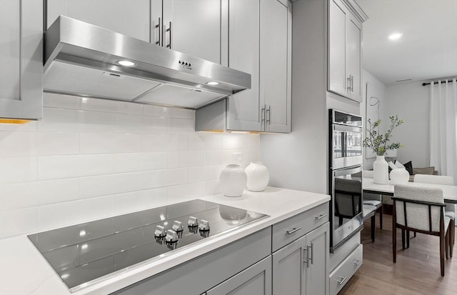 kitchen featuring ventilation hood, black electric cooktop, gray cabinetry, backsplash, and light wood-type flooring