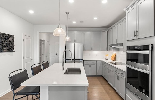 kitchen with appliances with stainless steel finishes, gray cabinetry, a sink, a breakfast bar area, and light countertops