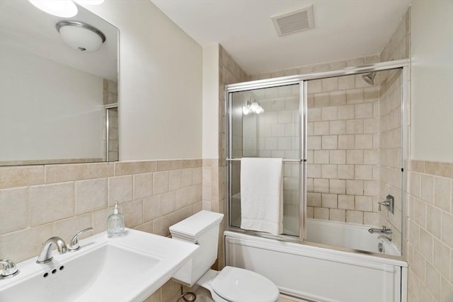 full bathroom with tile walls, a sink, combined bath / shower with glass door, and toilet