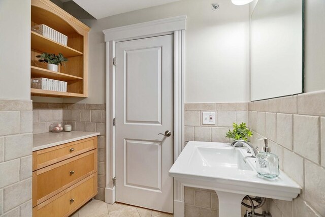 bathroom featuring tile walls, tile patterned flooring, wainscoting, and a sink