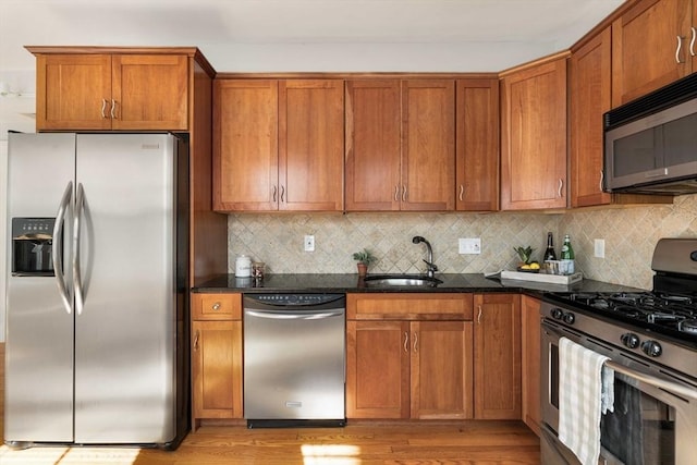 kitchen featuring stainless steel appliances, a sink, brown cabinetry, and tasteful backsplash