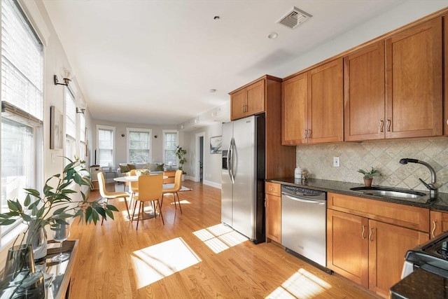 kitchen with appliances with stainless steel finishes, a sink, brown cabinets, light wood finished floors, and tasteful backsplash