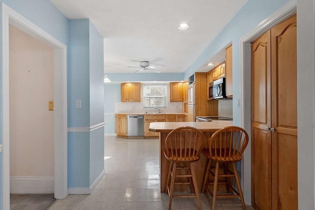 kitchen with baseboards, decorative backsplash, appliances with stainless steel finishes, a breakfast bar area, and a peninsula