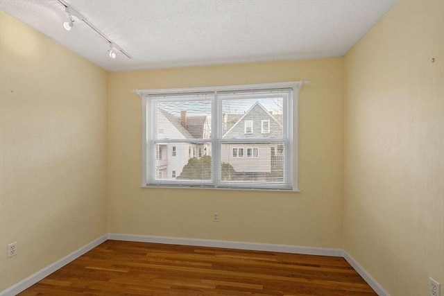 unfurnished room with a textured ceiling, wood finished floors, a wealth of natural light, and baseboards