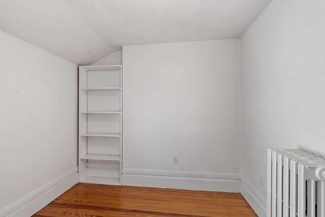 unfurnished bedroom featuring radiator heating unit, baseboards, vaulted ceiling, and wood finished floors