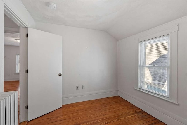 spare room with vaulted ceiling, baseboards, wood finished floors, and radiator