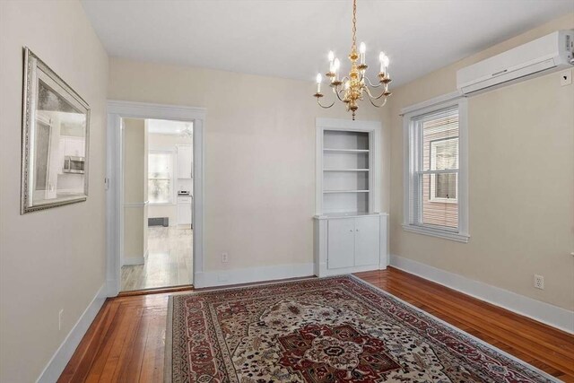 unfurnished dining area with built in features, a notable chandelier, hardwood / wood-style floors, a wall mounted air conditioner, and baseboards